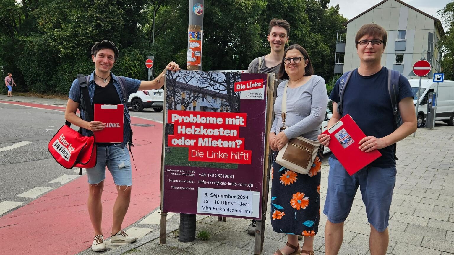 Das Foto zeigt 4 Genoss*innen der Linken mit Klemmbrettern in der Hand. Sie stehen neben einem Plakat, auf dem Die Linke auf das Hilfsangebot hinweist mit den Worten: Probleme mit Heizkosten oder Miete? Die Linke hilft.